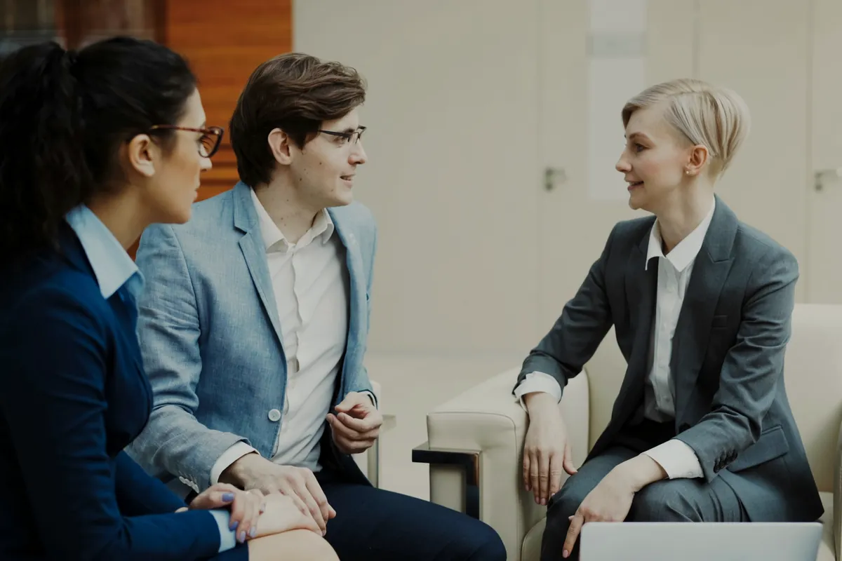 Three professionals talking and smiling in a modern office lounge